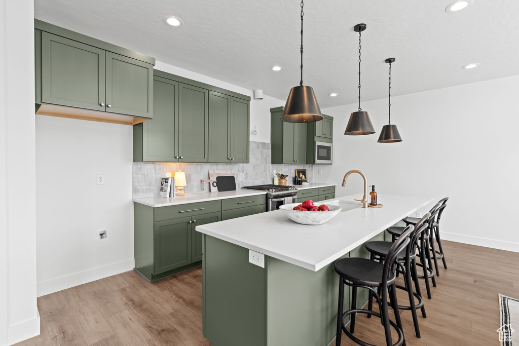 Kitchen with tasteful backsplash, appliances with stainless steel finishes, light hardwood / wood-style floors, sink, and green cabinets