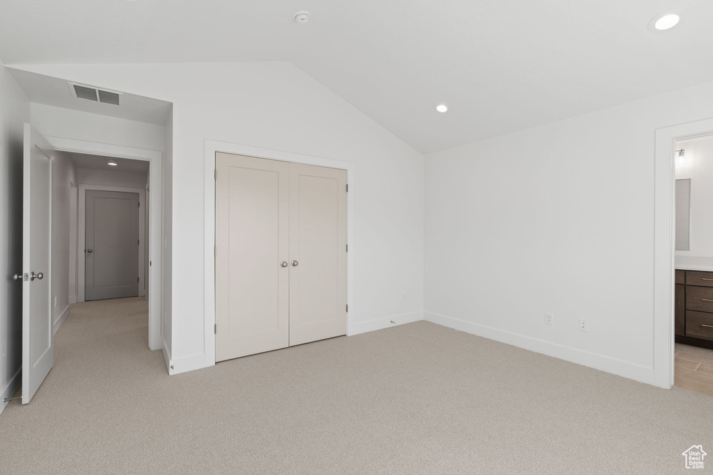 Unfurnished bedroom featuring a closet, vaulted ceiling, connected bathroom, and light carpet