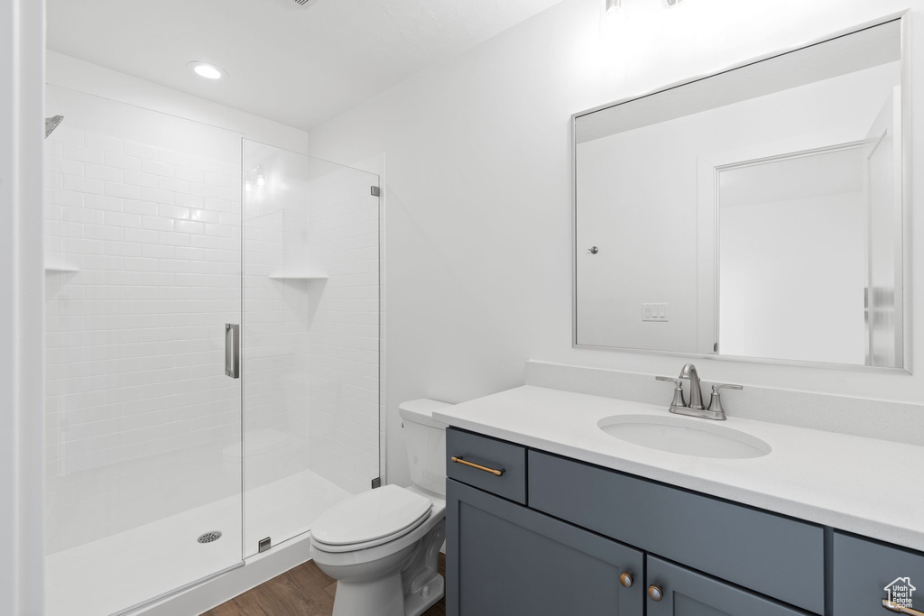 Bathroom featuring a shower with door, toilet, vanity, and wood-type flooring