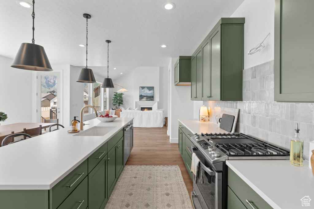 Kitchen featuring appliances with stainless steel finishes, backsplash, light hardwood / wood-style floors, sink, and green cabinetry