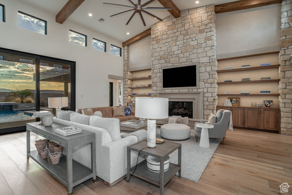 Living room with a stone fireplace, beamed ceiling, light hardwood / wood-style flooring, and a towering ceiling