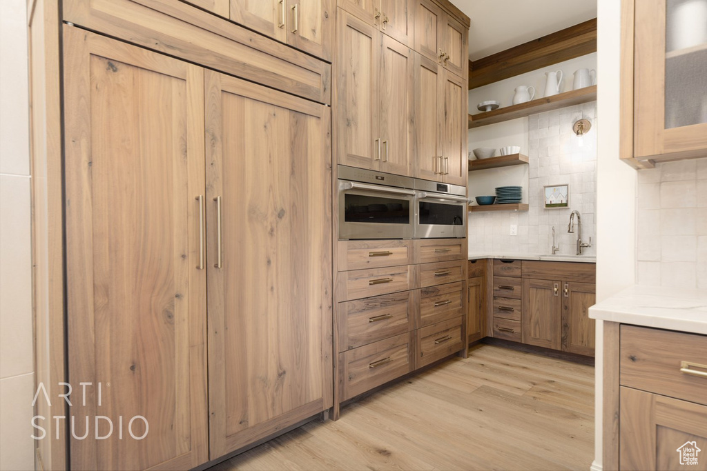 Kitchen featuring oven, sink, light hardwood / wood-style flooring, and backsplash