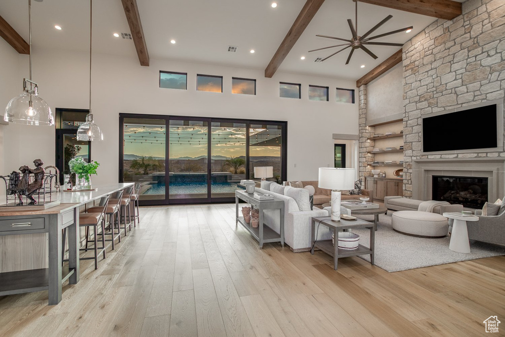 Living room featuring a fireplace, ceiling fan, beam ceiling, light hardwood / wood-style floors, and a towering ceiling