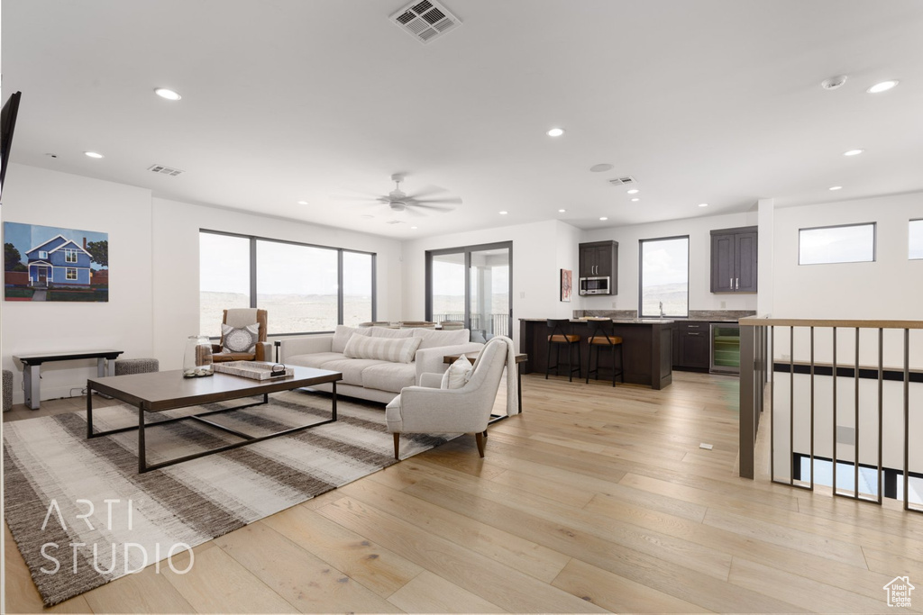 Living room with beverage cooler, light hardwood / wood-style floors, and ceiling fan