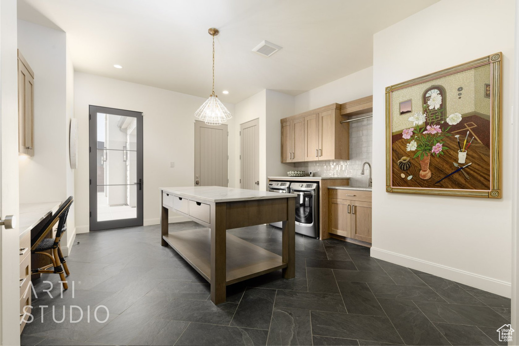 Kitchen featuring dark tile patterned floors, light brown cabinets, decorative backsplash, washer / dryer, and decorative light fixtures