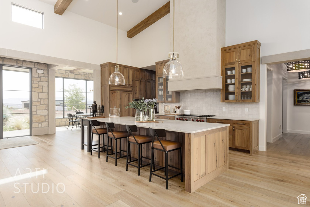 Kitchen with a breakfast bar area, beamed ceiling, decorative light fixtures, light wood-type flooring, and a center island