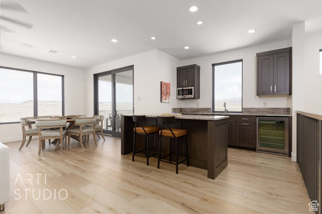 Kitchen featuring light hardwood / wood-style floors, a healthy amount of sunlight, a breakfast bar area, and wine cooler