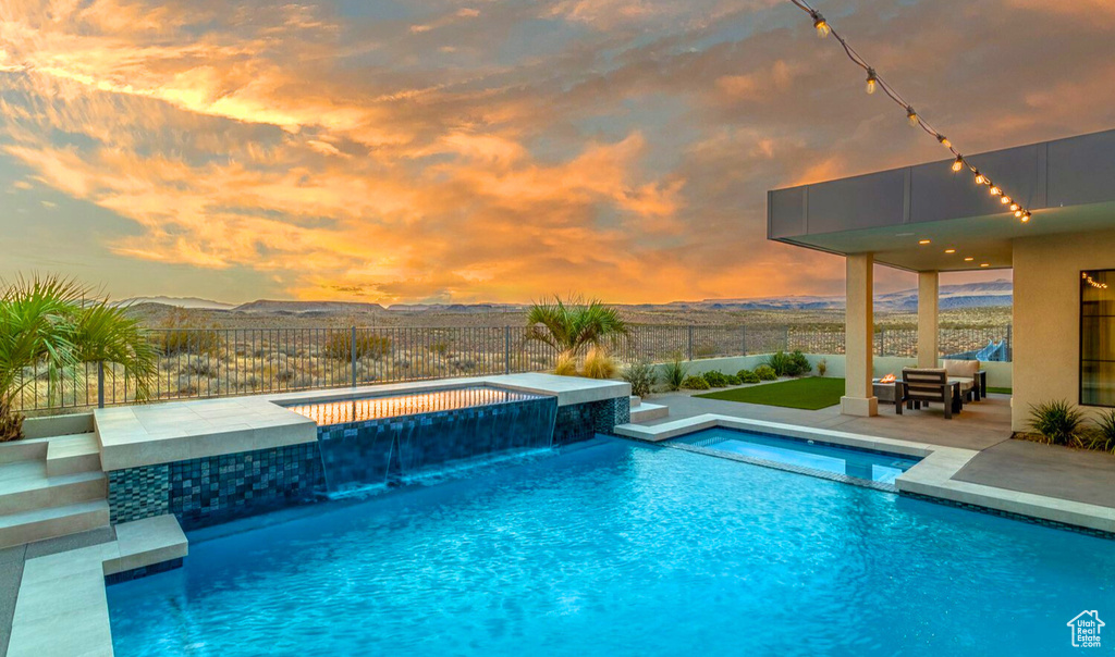 Pool at dusk with an in ground hot tub, pool water feature, a patio area, and a mountain view