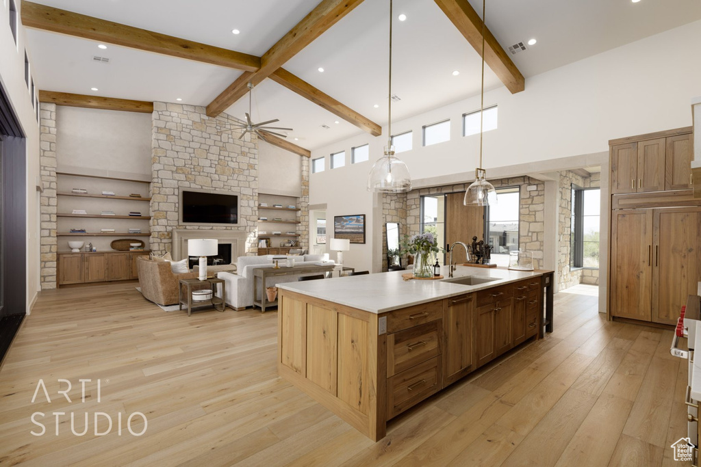 Kitchen with a center island with sink, sink, a fireplace, decorative light fixtures, and light wood-type flooring