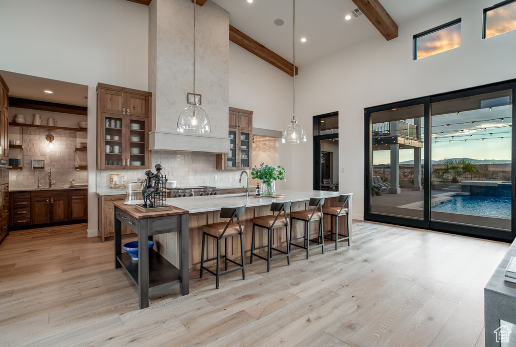 Kitchen with light hardwood / wood-style flooring, pendant lighting, backsplash, a kitchen breakfast bar, and high vaulted ceiling