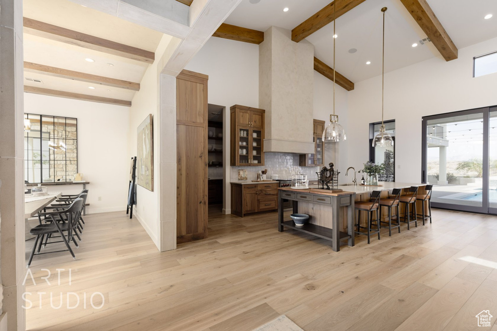 Kitchen featuring hanging light fixtures, decorative backsplash, a center island with sink, light hardwood / wood-style flooring, and a kitchen breakfast bar