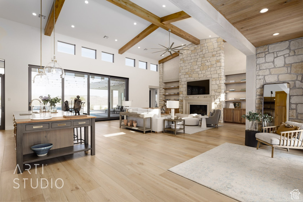 Living room featuring beam ceiling, light hardwood / wood-style flooring, a high ceiling, ceiling fan with notable chandelier, and a fireplace