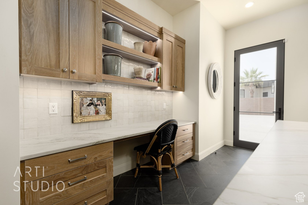 Home office with dark tile patterned floors and built in desk