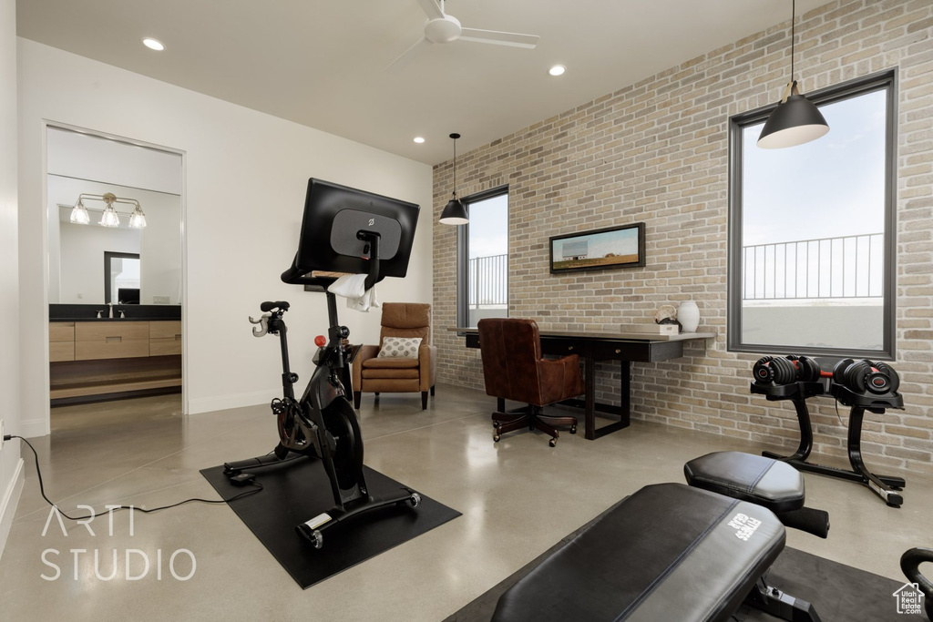 Exercise area featuring brick wall, concrete flooring, and ceiling fan