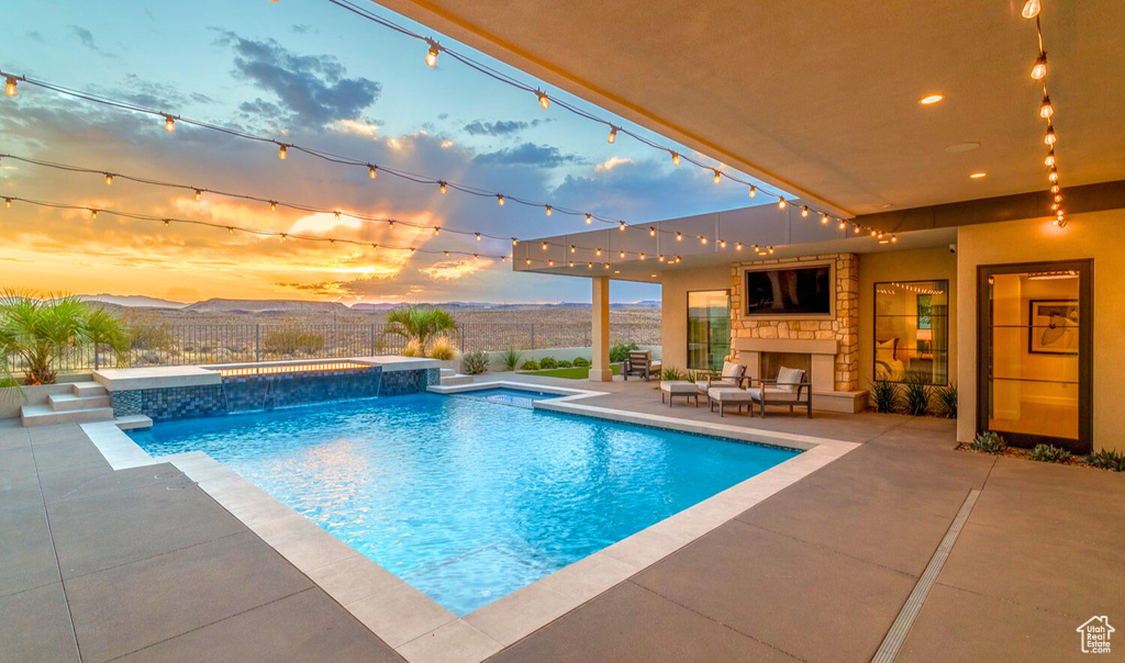 Pool at dusk featuring pool water feature, a patio area, and an outdoor stone fireplace