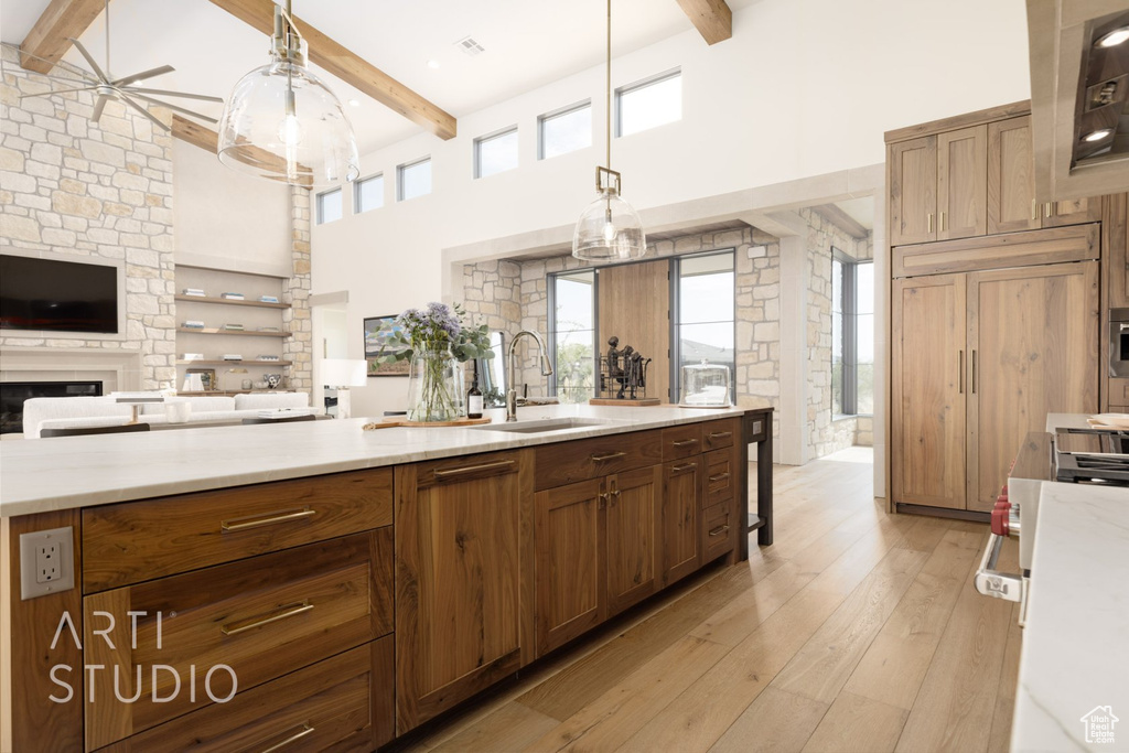 Kitchen with beamed ceiling, sink, light hardwood / wood-style flooring, and hanging light fixtures