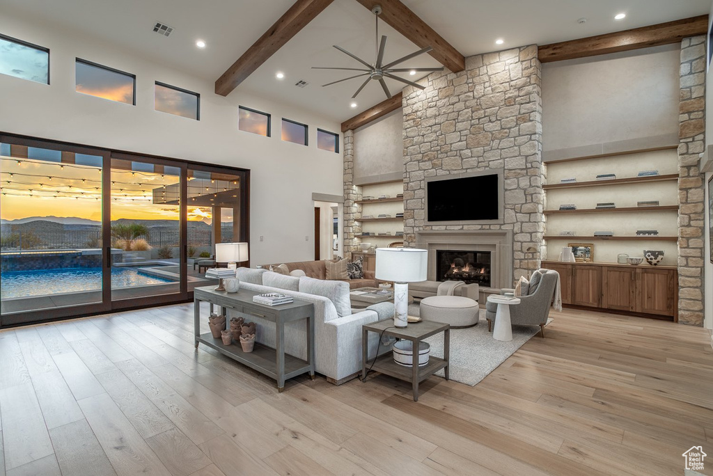 Living room featuring beam ceiling, a stone fireplace, light wood-type flooring, and a high ceiling