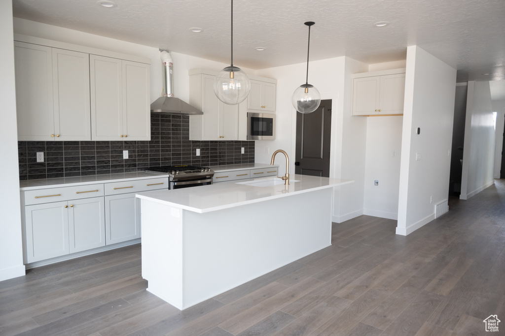 Kitchen featuring sink, appliances with stainless steel finishes, a center island with sink, wall chimney range hood, and white cabinets