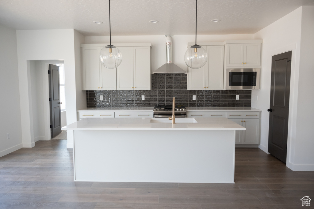 Kitchen featuring wall chimney range hood, decorative light fixtures, a center island with sink, and appliances with stainless steel finishes