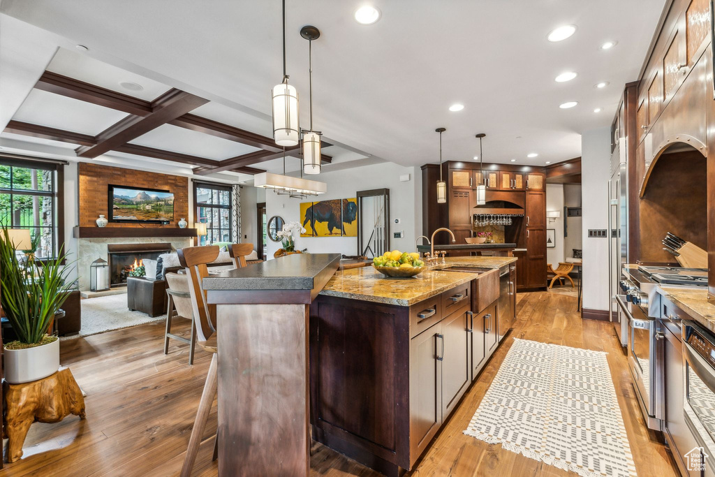 Kitchen featuring decorative light fixtures, light wood-type flooring, an island with sink, beam ceiling, and coffered ceiling