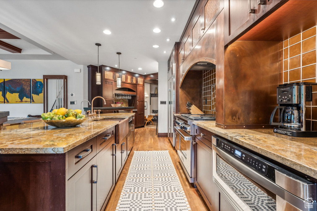 Kitchen with a center island with sink, light hardwood / wood-style floors, decorative light fixtures, dishwasher, and high end stainless steel range