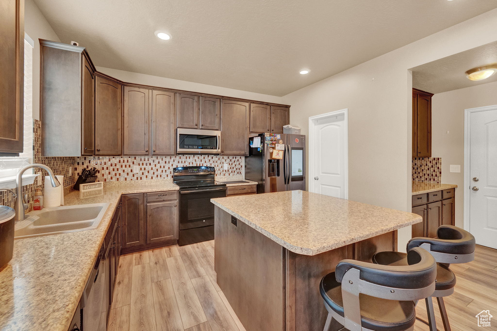 Kitchen with decorative backsplash, light hardwood / wood-style floors, appliances with stainless steel finishes, and sink