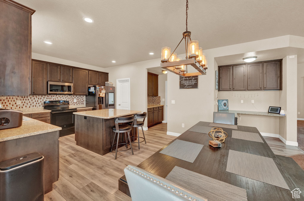 Kitchen featuring dark brown cabinets, stainless steel appliances, decorative backsplash, a center island, and light hardwood / wood-style flooring