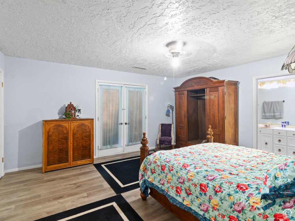 Bedroom with light hardwood / wood-style floors, sink, ensuite bath, and a textured ceiling