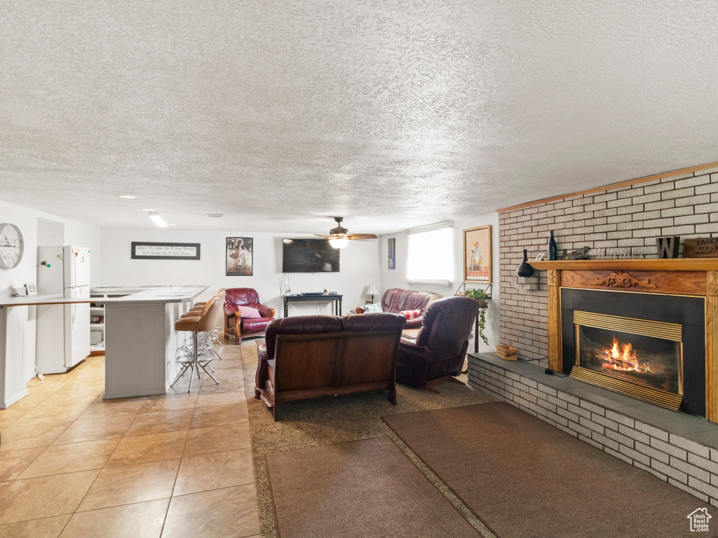 Living room featuring light tile patterned flooring, a textured ceiling, ceiling fan, brick wall, and a fireplace