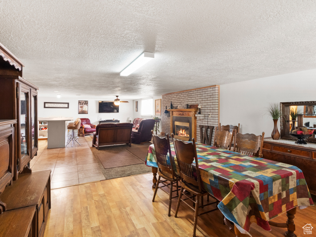 Dining area featuring a brick fireplace, brick wall, light wood-type flooring, and a textured ceiling