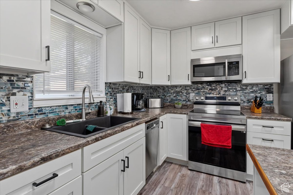 Kitchen featuring white cabinets, backsplash, stainless steel appliances, light hardwood / wood-style floors, and sink