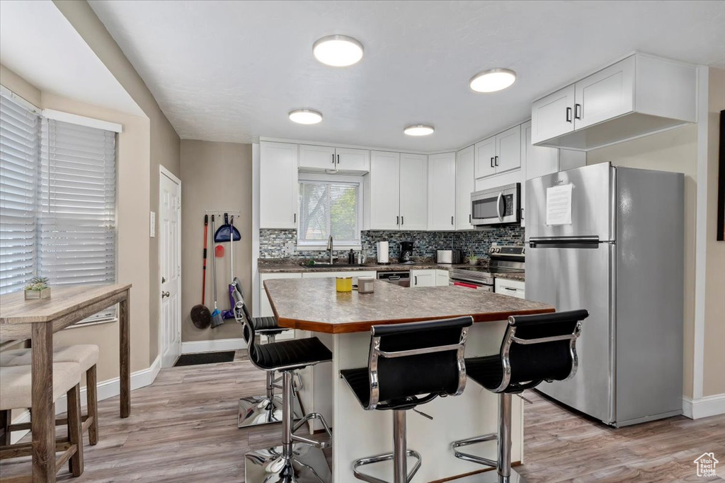 Kitchen featuring light hardwood / wood-style flooring, a center island, tasteful backsplash, and stainless steel appliances