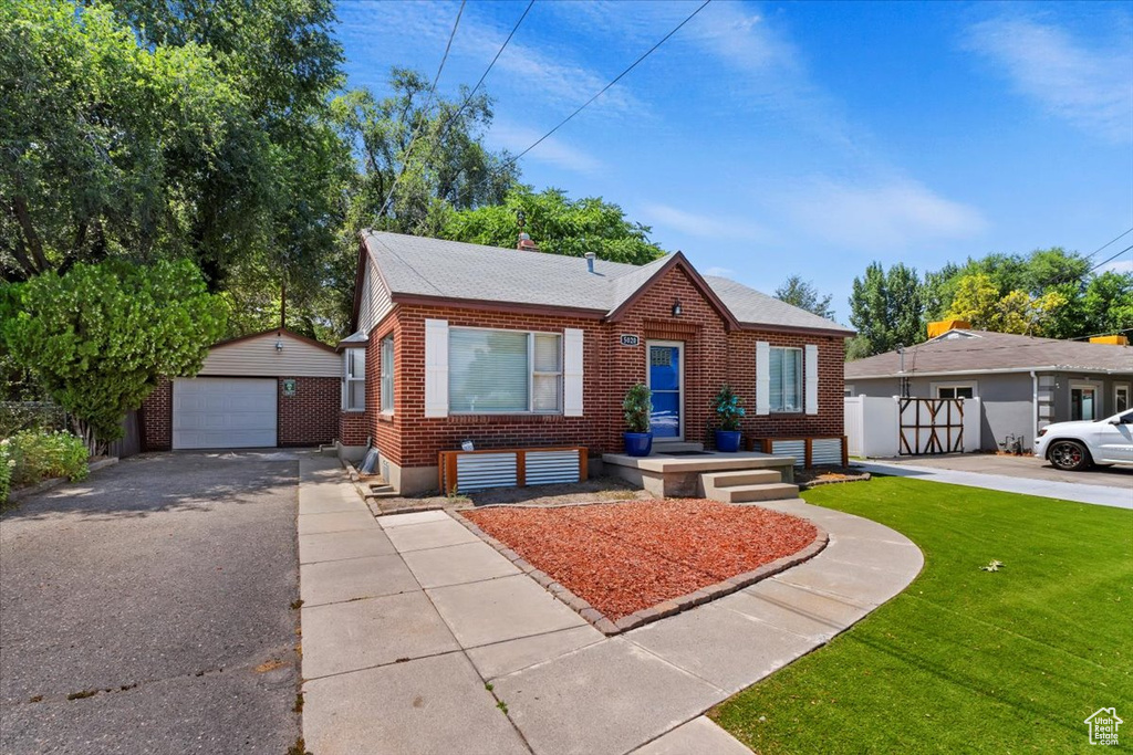 Bungalow-style home with a garage, an outdoor structure, and a front lawn