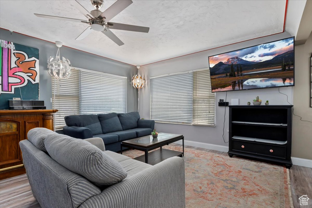 Living room with ceiling fan with notable chandelier and hardwood / wood-style floors