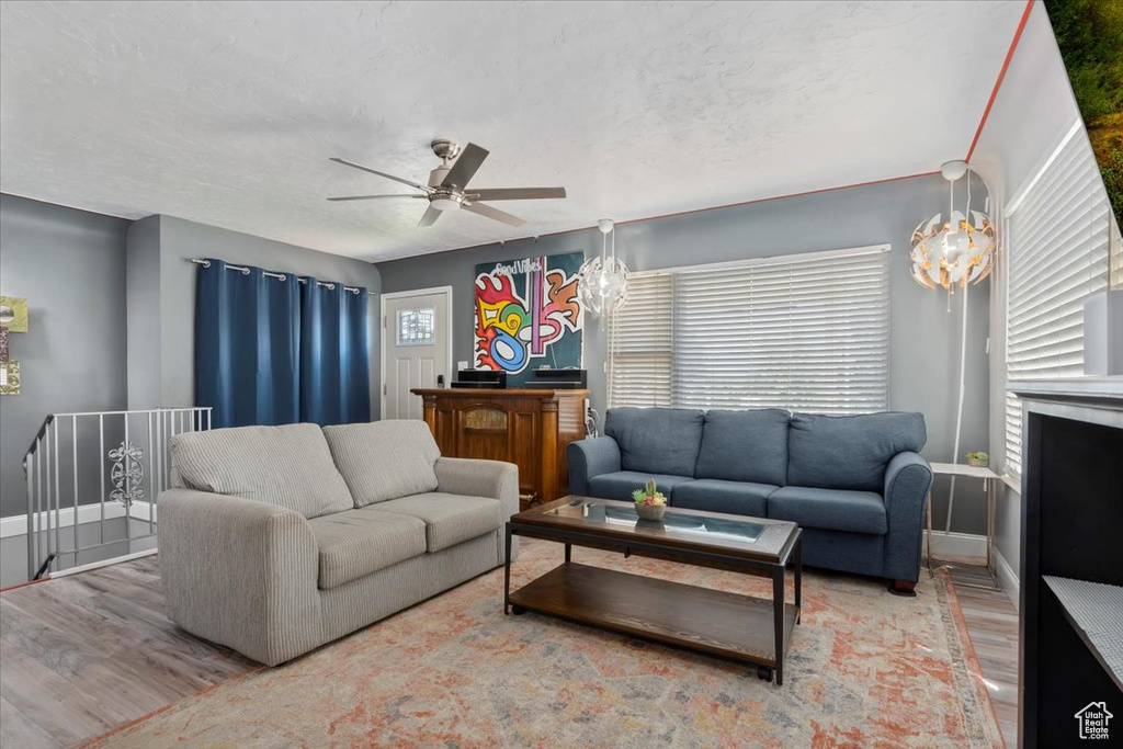 Living room featuring a textured ceiling, wood-type flooring, and ceiling fan with notable chandelier