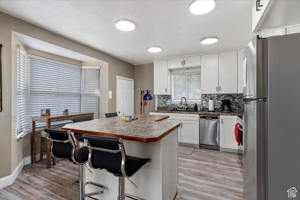 Kitchen featuring tasteful backsplash, white cabinets, a center island, appliances with stainless steel finishes, and sink