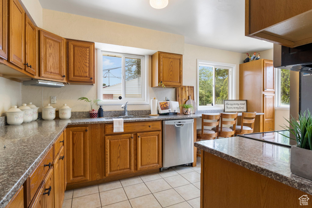 Kitchen featuring dark stone counters, sink, light tile patterned floors, stainless steel dishwasher, and black electric cooktop