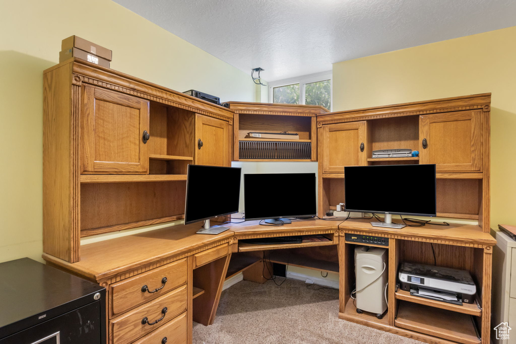 Office space with built in desk, vaulted ceiling, light colored carpet, and a textured ceiling