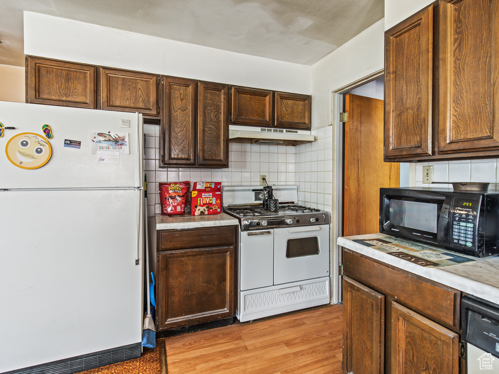 Kitchen with backsplash, light hardwood / wood-style floors, and white appliances