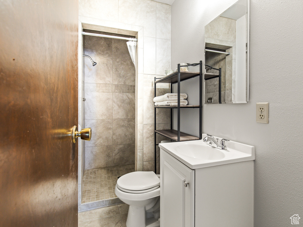 Bathroom featuring tile patterned flooring, toilet, vanity, and tiled shower