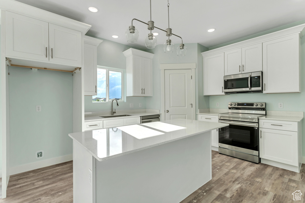 Kitchen with stainless steel appliances, sink, light hardwood / wood-style floors, a center island, and white cabinetry