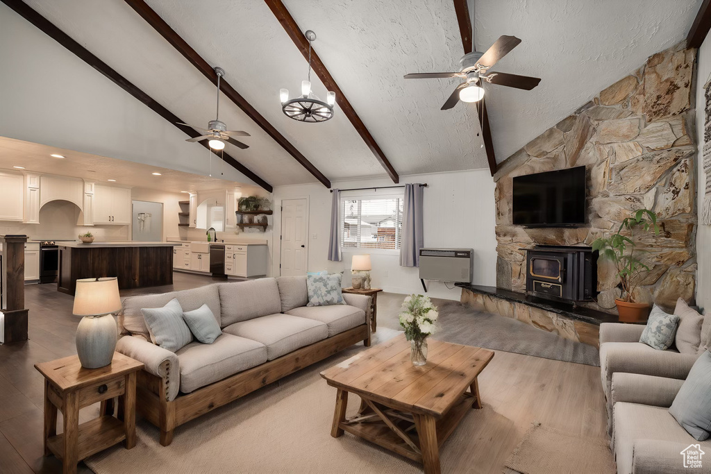 Living room featuring lofted ceiling with beams, ceiling fan with notable chandelier, wood-type flooring, and a wood stove