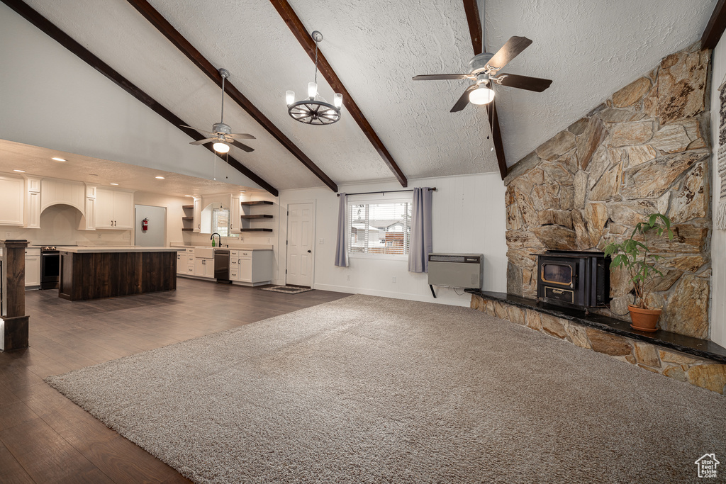 Unfurnished living room with beam ceiling, a wood stove, a textured ceiling, dark wood-type flooring, and ceiling fan with notable chandelier