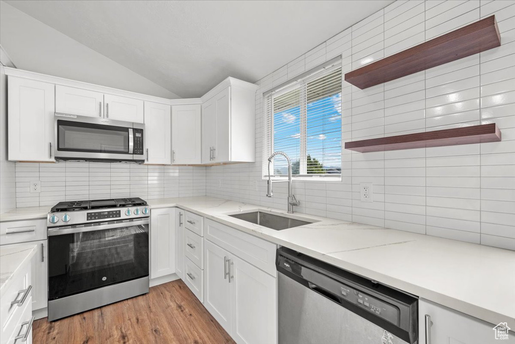 Kitchen with lofted ceiling, tasteful backsplash, white cabinets, stainless steel appliances, and sink