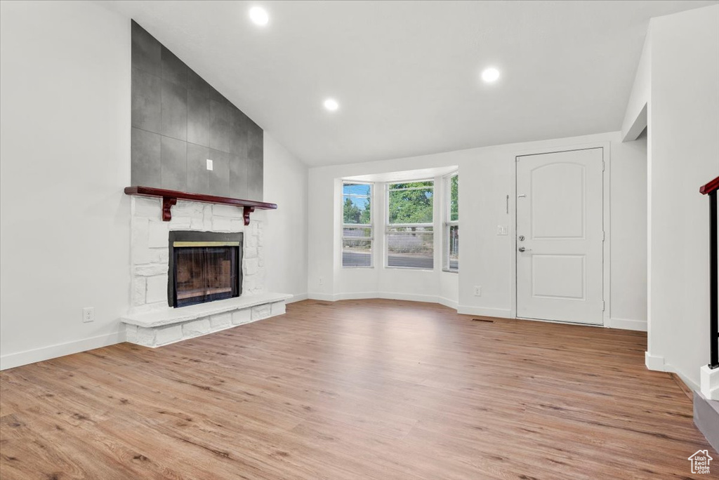 Unfurnished living room featuring high vaulted ceiling, a fireplace, and light wood-type flooring