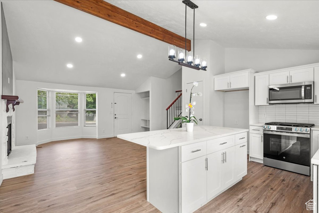 Kitchen with light hardwood / wood-style floors, beam ceiling, light stone countertops, and stainless steel appliances