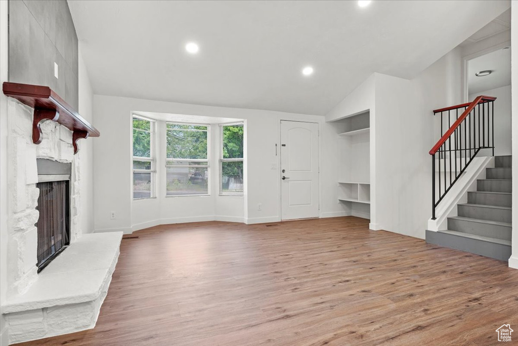 Unfurnished living room with a large fireplace, wood-type flooring, and lofted ceiling