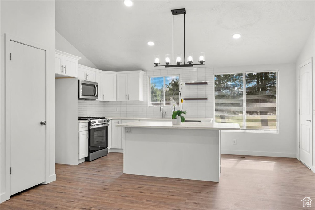 Kitchen with appliances with stainless steel finishes, tasteful backsplash, vaulted ceiling, hanging light fixtures, and light hardwood / wood-style floors