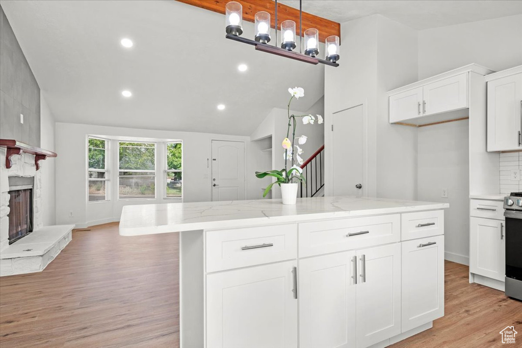 Kitchen featuring a stone fireplace, light stone counters, pendant lighting, light hardwood / wood-style floors, and white cabinetry