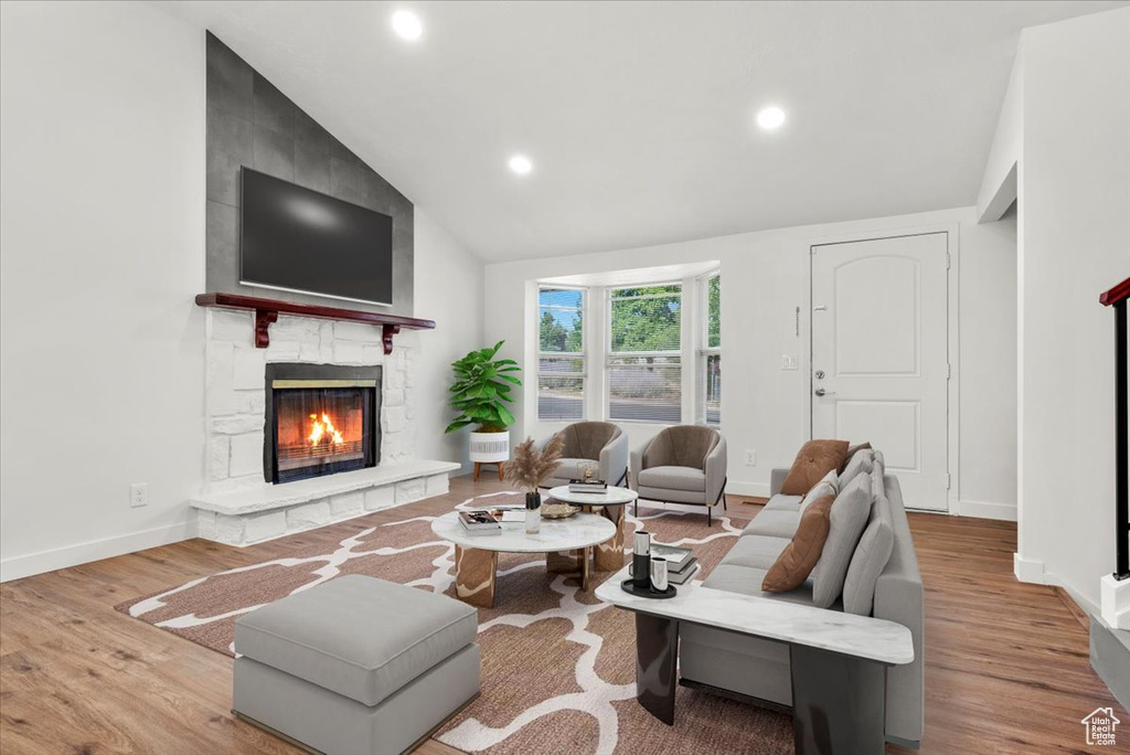 Living room featuring a stone fireplace, hardwood / wood-style flooring, and lofted ceiling